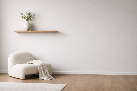 Small wall styled with a floating shelf, a single vase, and a lounge chair with soft fabric, creating a clean and visually complete space.
