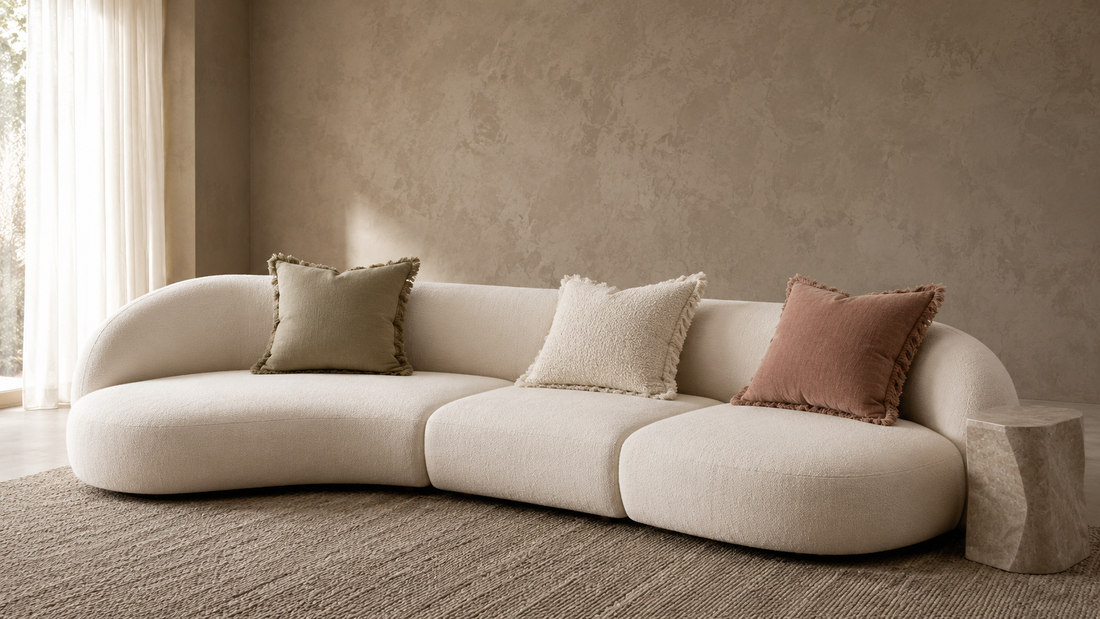 Curved minimal sofa with relaxed fringe-edge pillows creating balanced and comfortable seating depth.